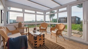 Une véranda meublée de mobilier en osier, avec une malle en bois et une vue sur la ville et la verdure.