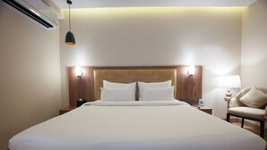 A hotel room with a large bed, a wooden headboard, two bedside lamps, a nightstand, and a chair. - Udman by Ferns N Petals Gurugram (Gurugram)