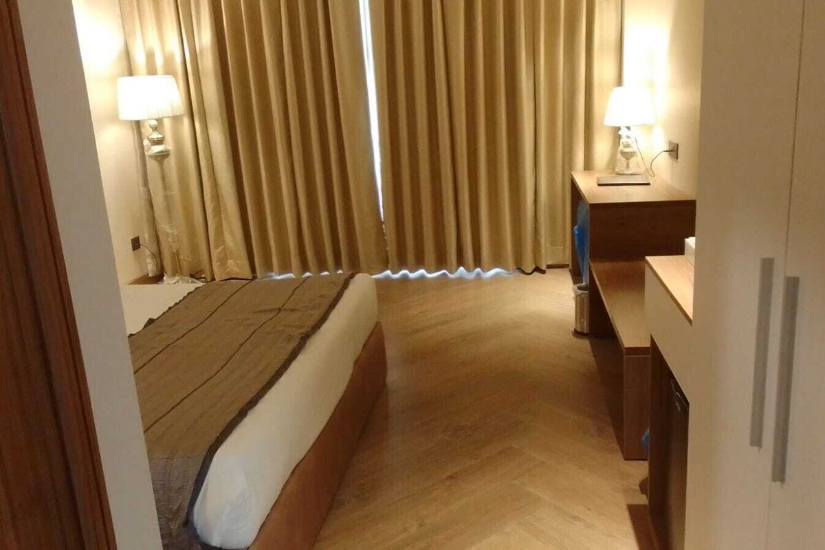 A hotel room with a bed, a desk, a lamp, and curtains.