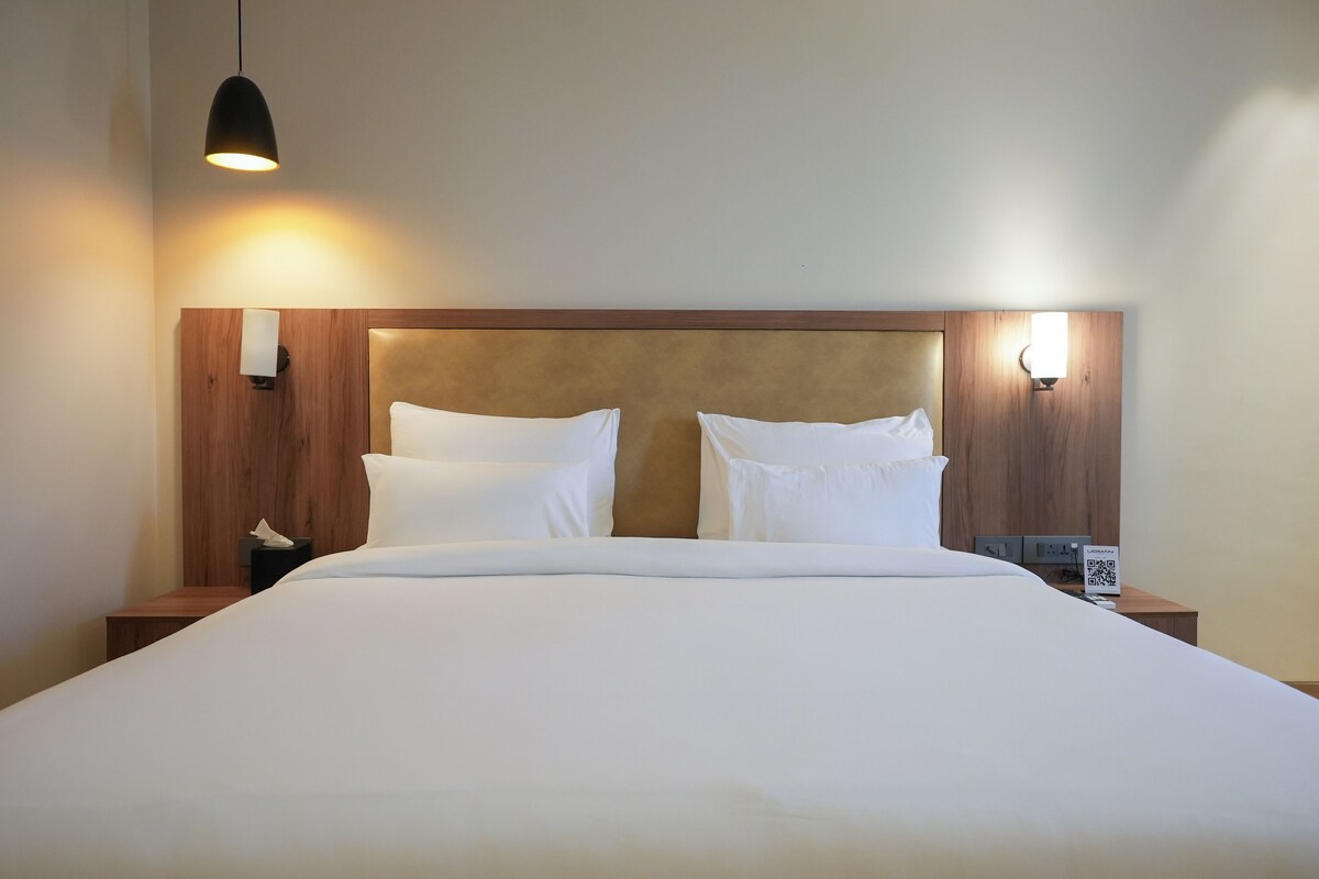 A neatly made bed with white linens, two bedside tables with lamps, and a wooden headboard.