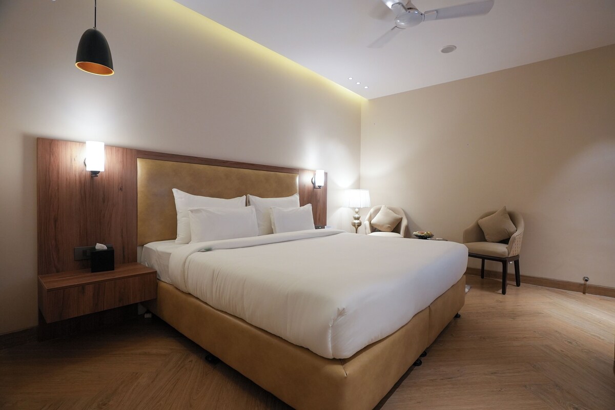 A modern hotel room with a large bed, wooden headboard, bedside tables, a chair, and a ceiling fan.