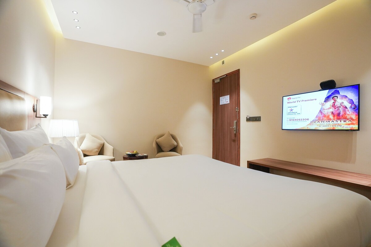 A hotel room with a bed, a TV on the wall, a desk, and a chair.