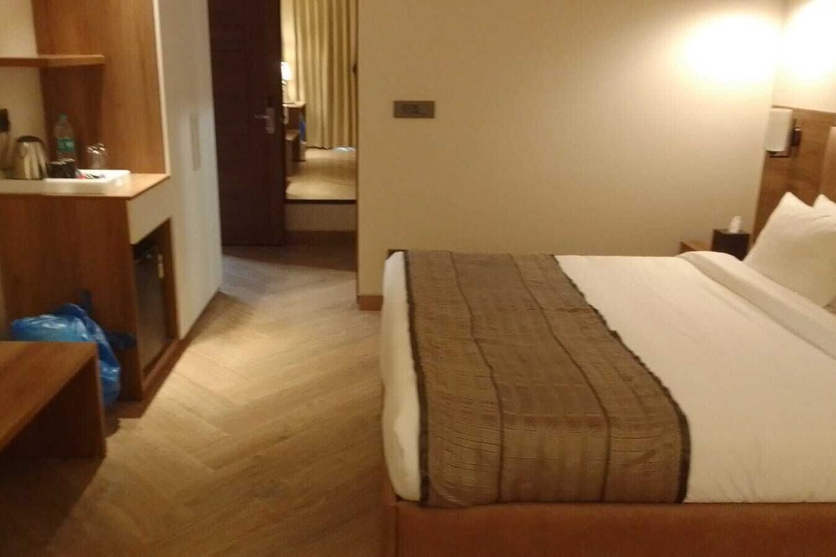 A hotel room with a bed, bedside table, and a small desk with a chair.
