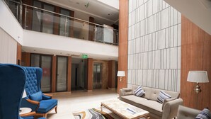 A spacious lobby with a high ceiling, a central seating area with sofas and armchairs, and a modern design with wood paneling and a marble floor. - Udman by Ferns N Petals Gurugram (Gurugram)