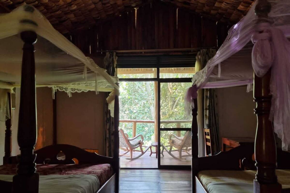 A room with two wooden beds, a large sliding glass door leading to an outdoor area with chairs.