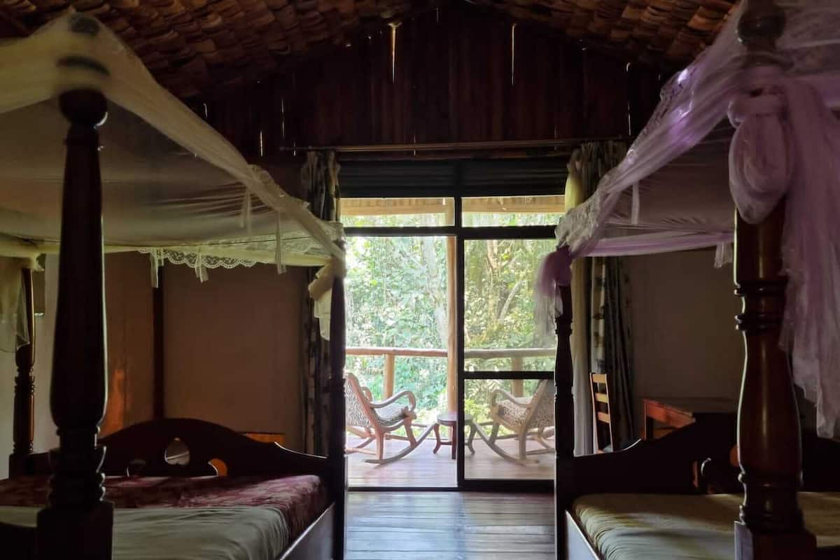 A room with two wooden beds, a large sliding glass door leading to an outdoor area with chairs.