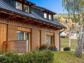 Ein modernes Holzhaus mit Satteldach, großen Fenstern und Blick auf einen bewaldeten Hang.