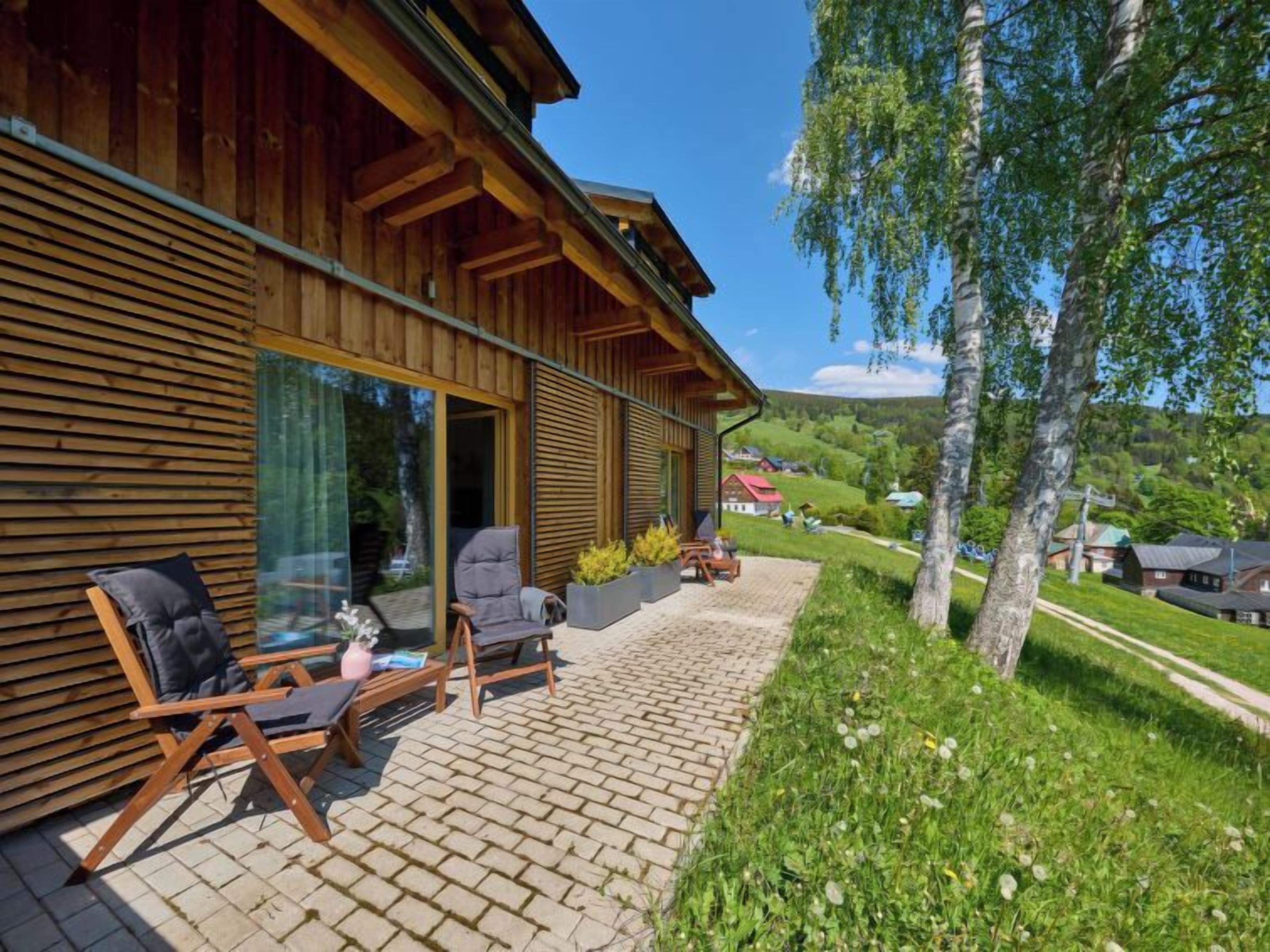 Une cabane en bois dotée d’un patio comprenant deux chaises et une table, offrant une vue sur un paysage verdoyant et luxuriant.