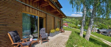 Une cabane en bois dotée d’un patio comprenant deux chaises et une table, offrant une vue sur un paysage verdoyant et luxuriant.