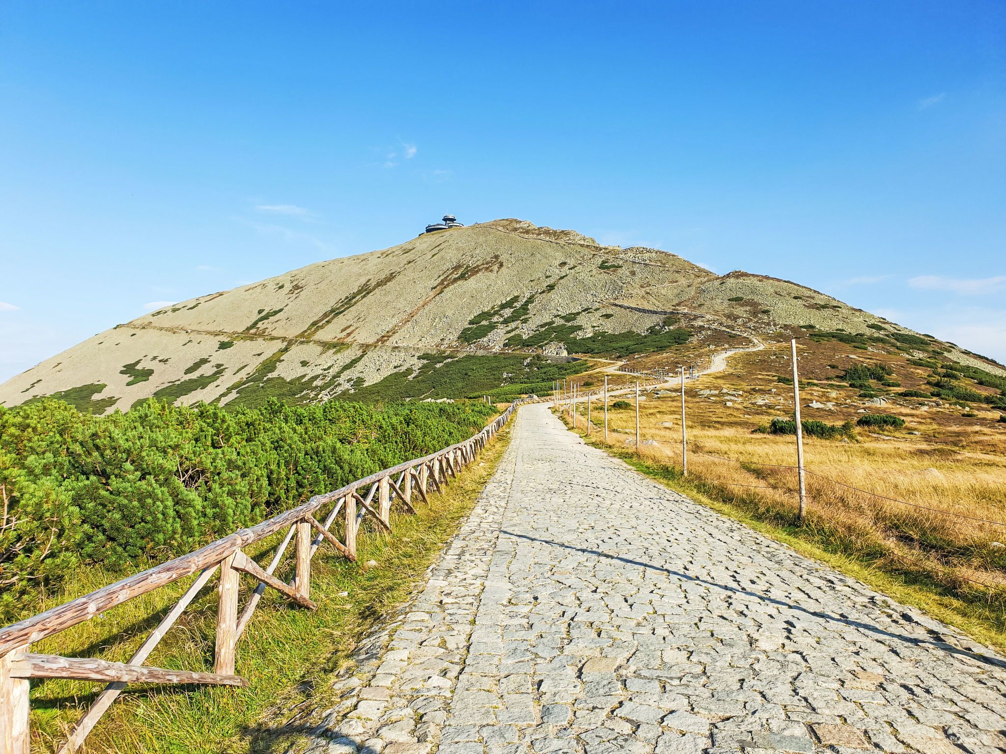 A paved pathway leading to a mountain with a wooden fence on one side.