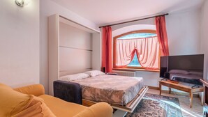 A hotel room with a bed, a TV, a sofa, and a window with curtains. - Casa Nota e Minichin by Interhome (Pré Saint Didier)