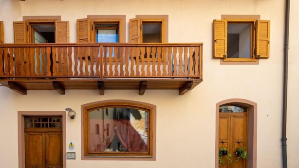 A building with a wooden balcony, a double wooden door, and a window with a curtain. - Casa Nota e Minichin by Interhome (Pré Saint Didier)