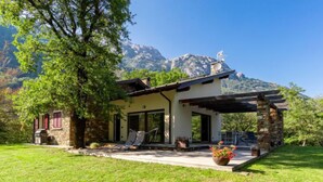 Ein zweistöckiges Haus mit Naturstein-Fassade, einer Veranda und Blick auf Berge.