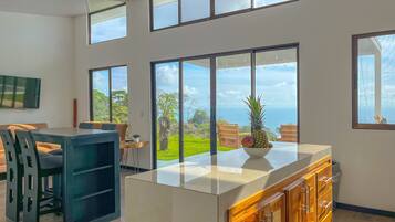 A modern kitchen with large windows, a dining area with a table and chairs, and a view of the outdoors.