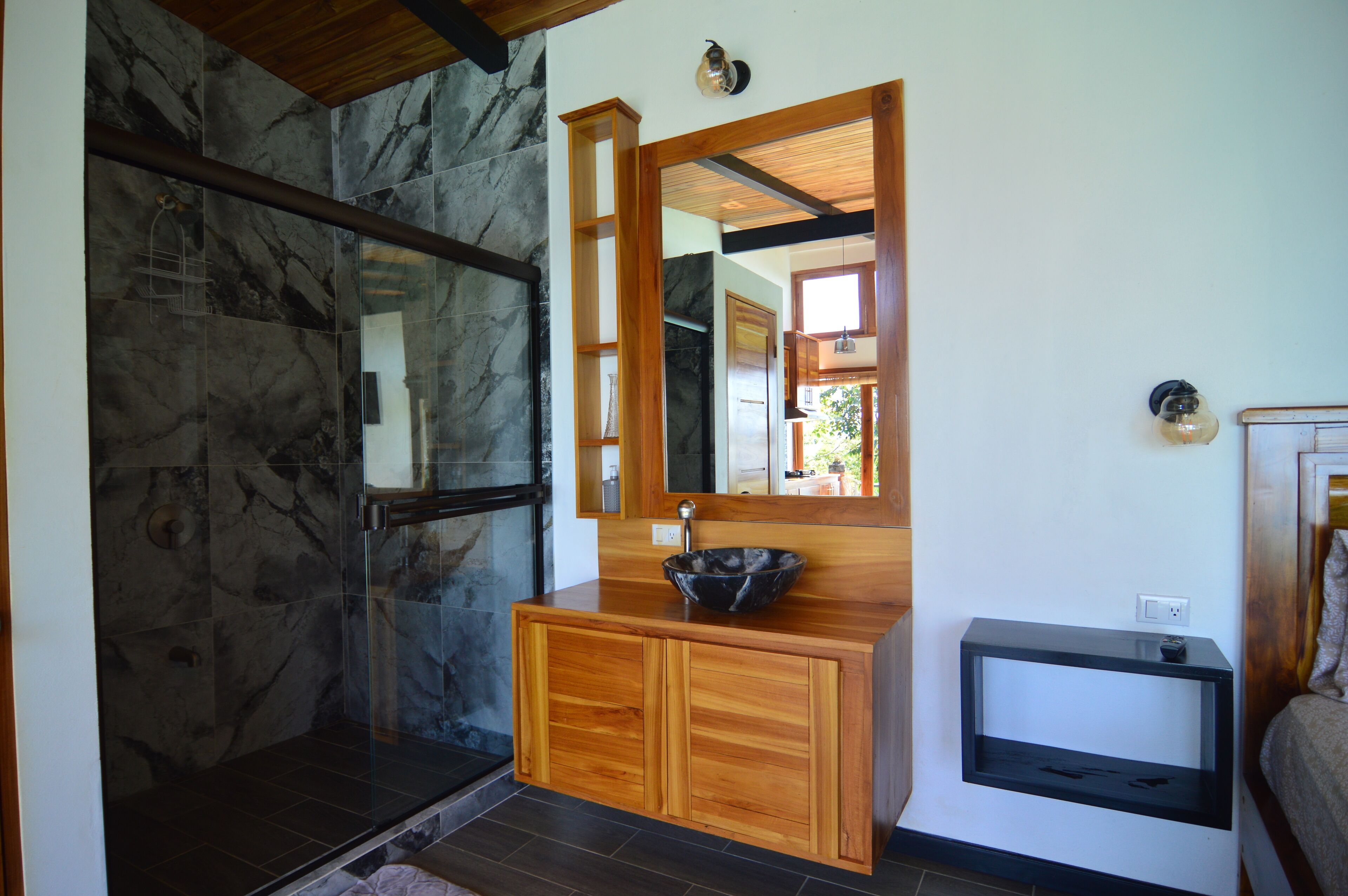 A bathroom with a stone shower, wooden vanity, and a mirror.