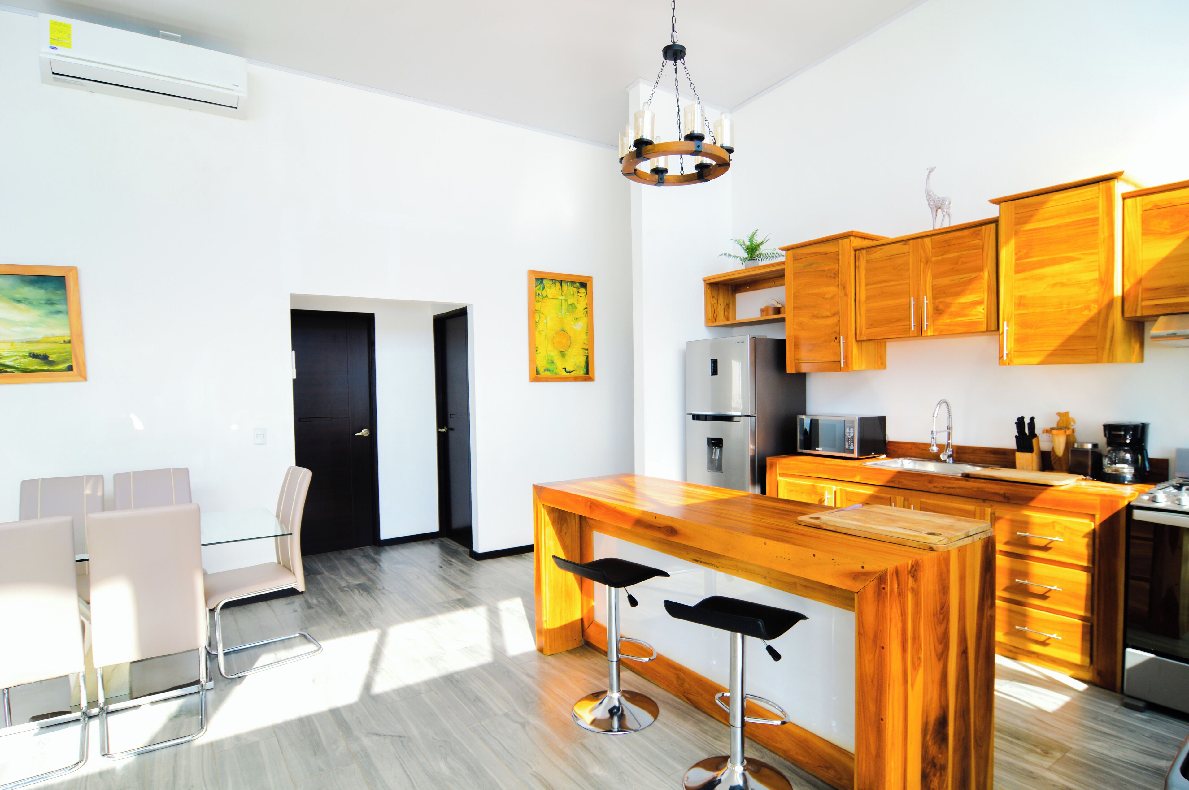 A modern kitchen with wooden cabinets, a central island with bar stools, a refrigerator, and a microwave.