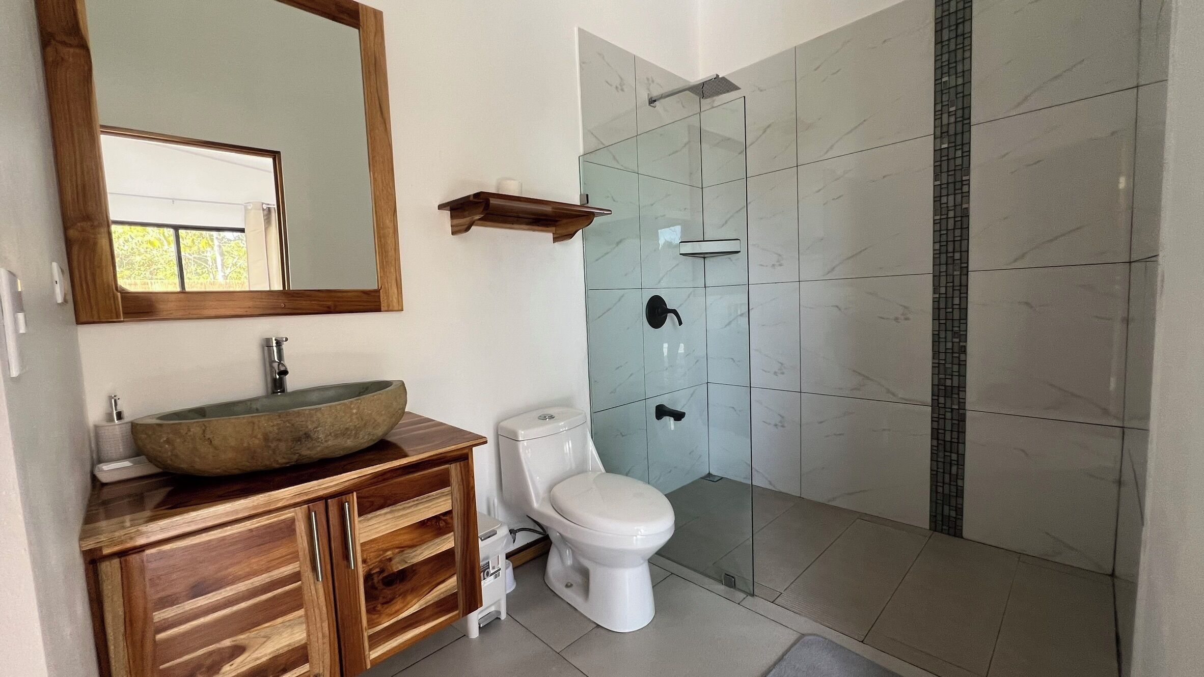 A modern bathroom with a wooden vanity, a large mirror, a vessel sink, a toilet, and a glass shower enclosure.