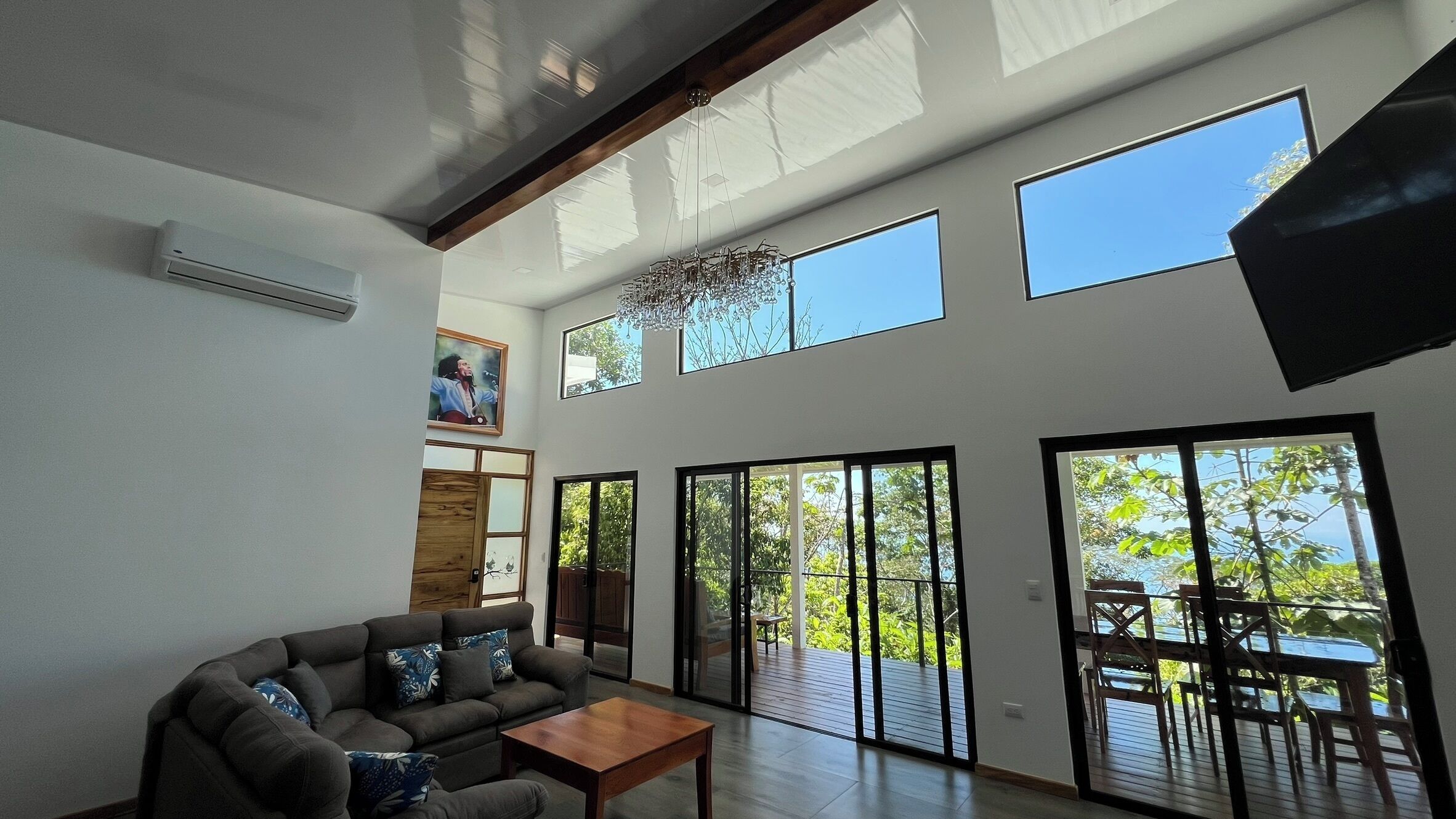 A spacious living room with a sofa, coffee table, and large windows offering views of greenery.