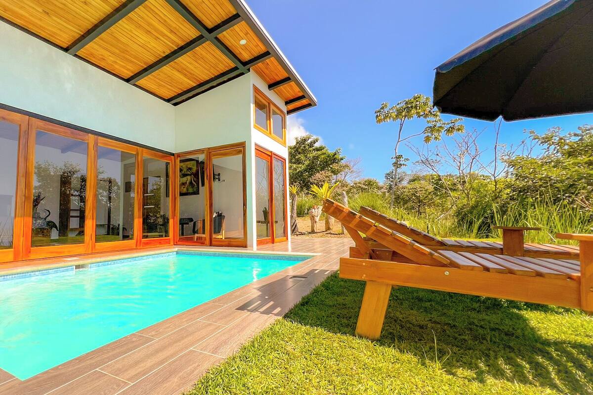 A modern house with a swimming pool, large glass doors, and a wooden deck.