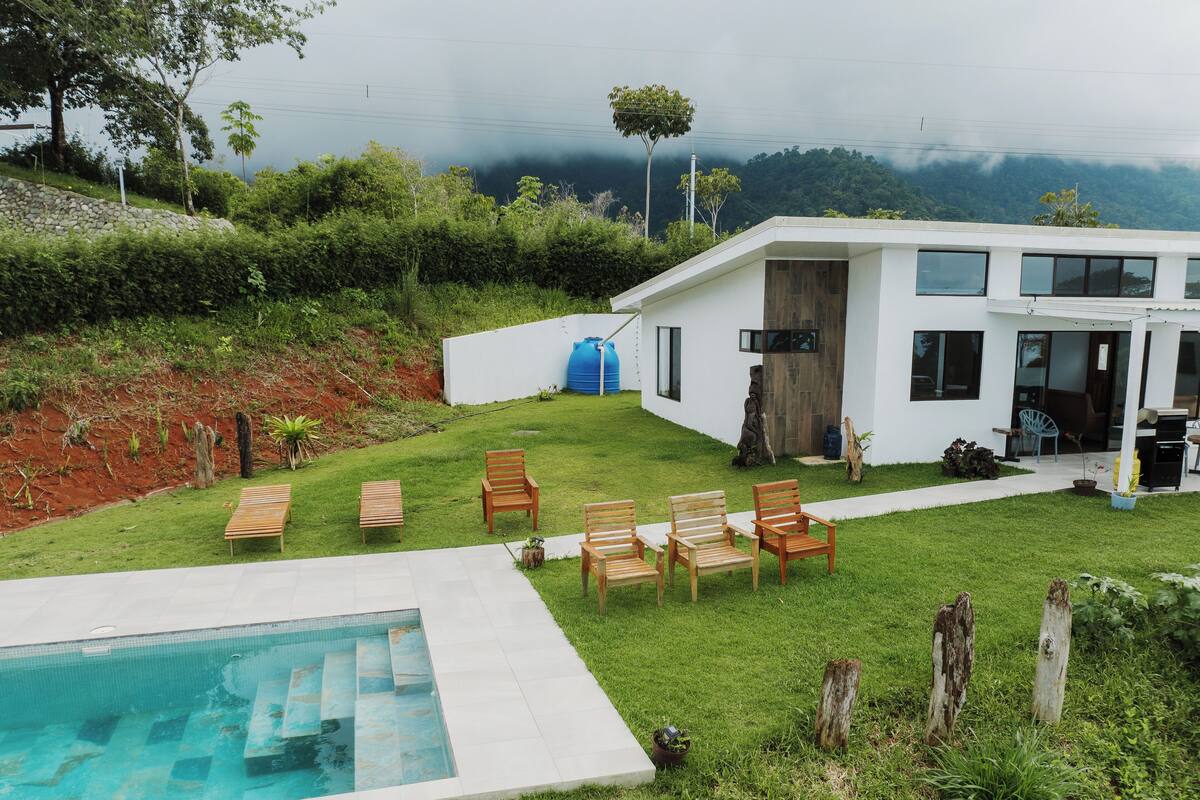 A modern house with a swimming pool, outdoor seating, and a view of a mountainous landscape.