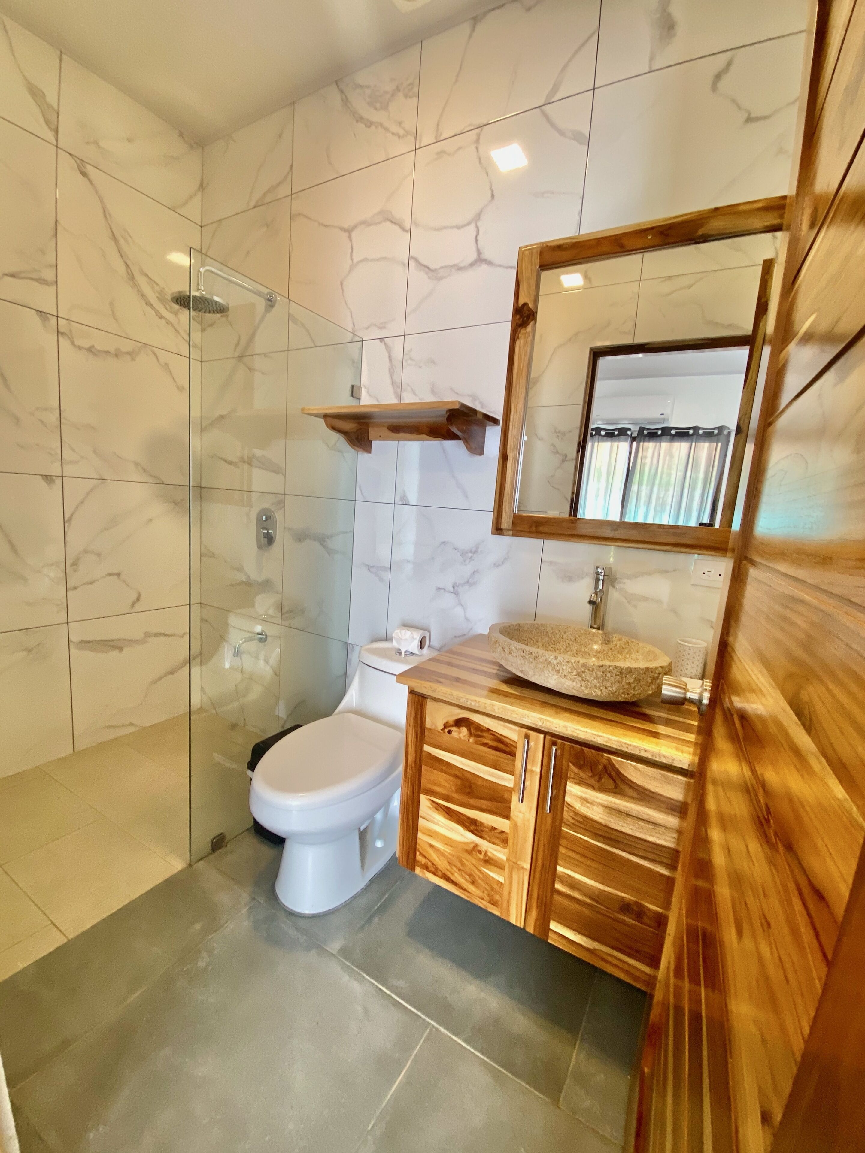 Un baño moderno con ducha de vidrio, tocador de madera con lavamanos y un inodoro.