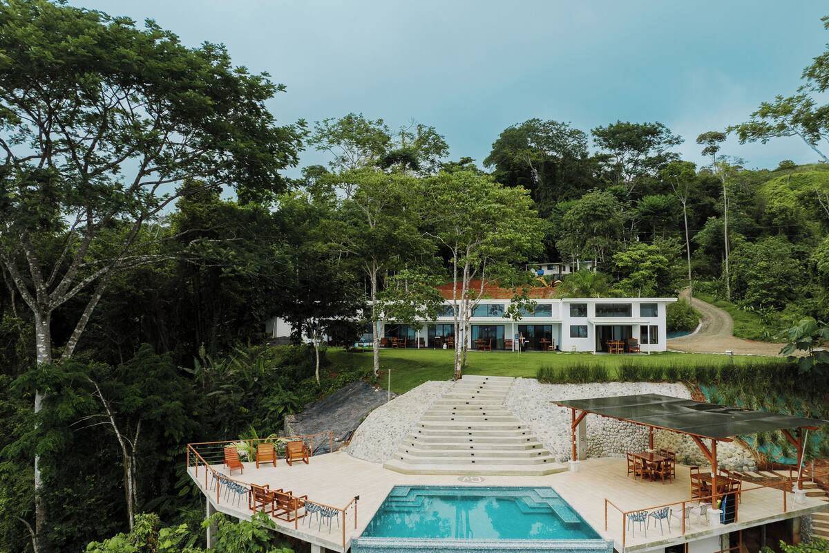 A modern resort with a pool, outdoor seating, and a view of the surrounding forest.