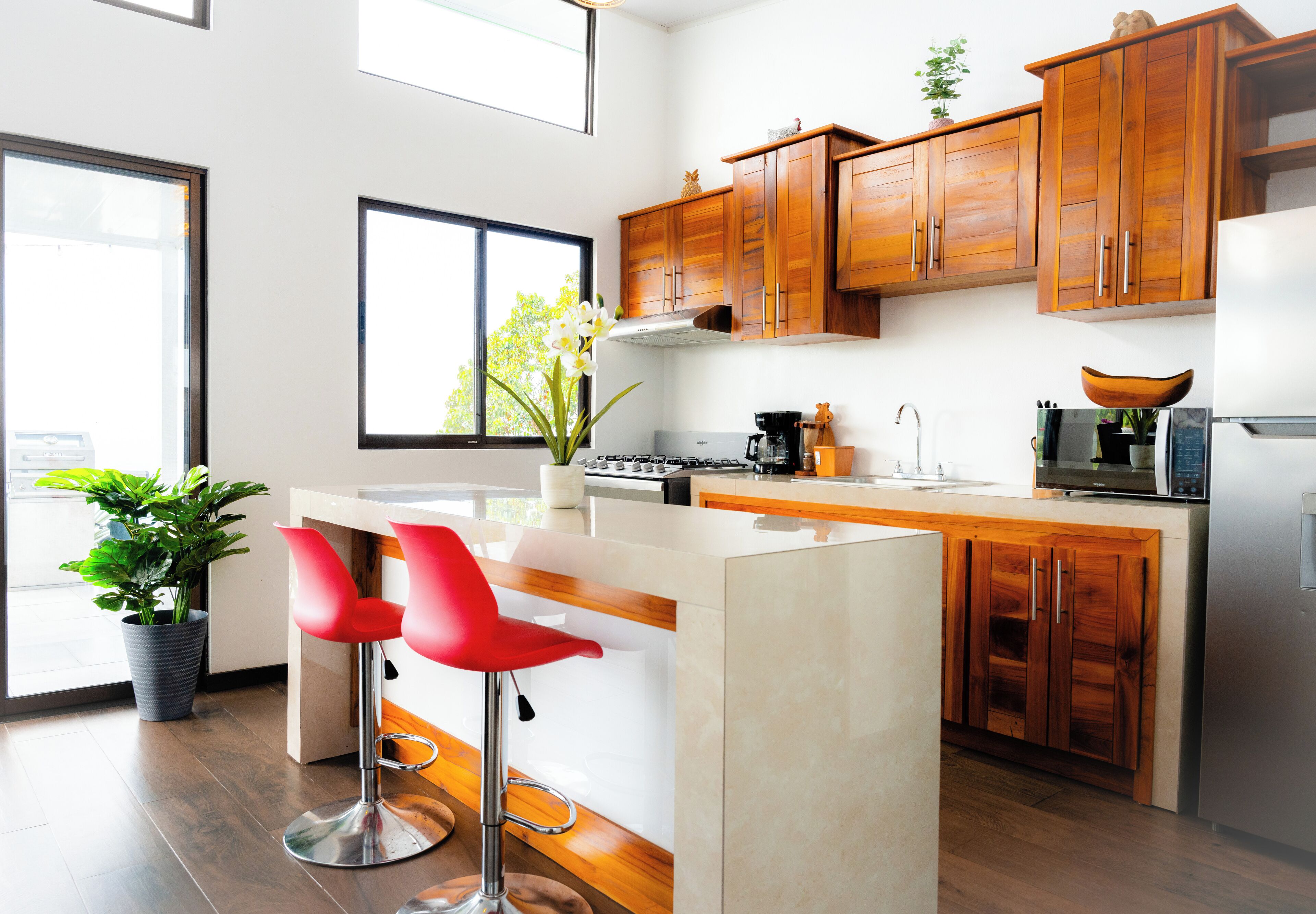 A modern kitchen with wooden cabinets, a central island, and red bar stools.