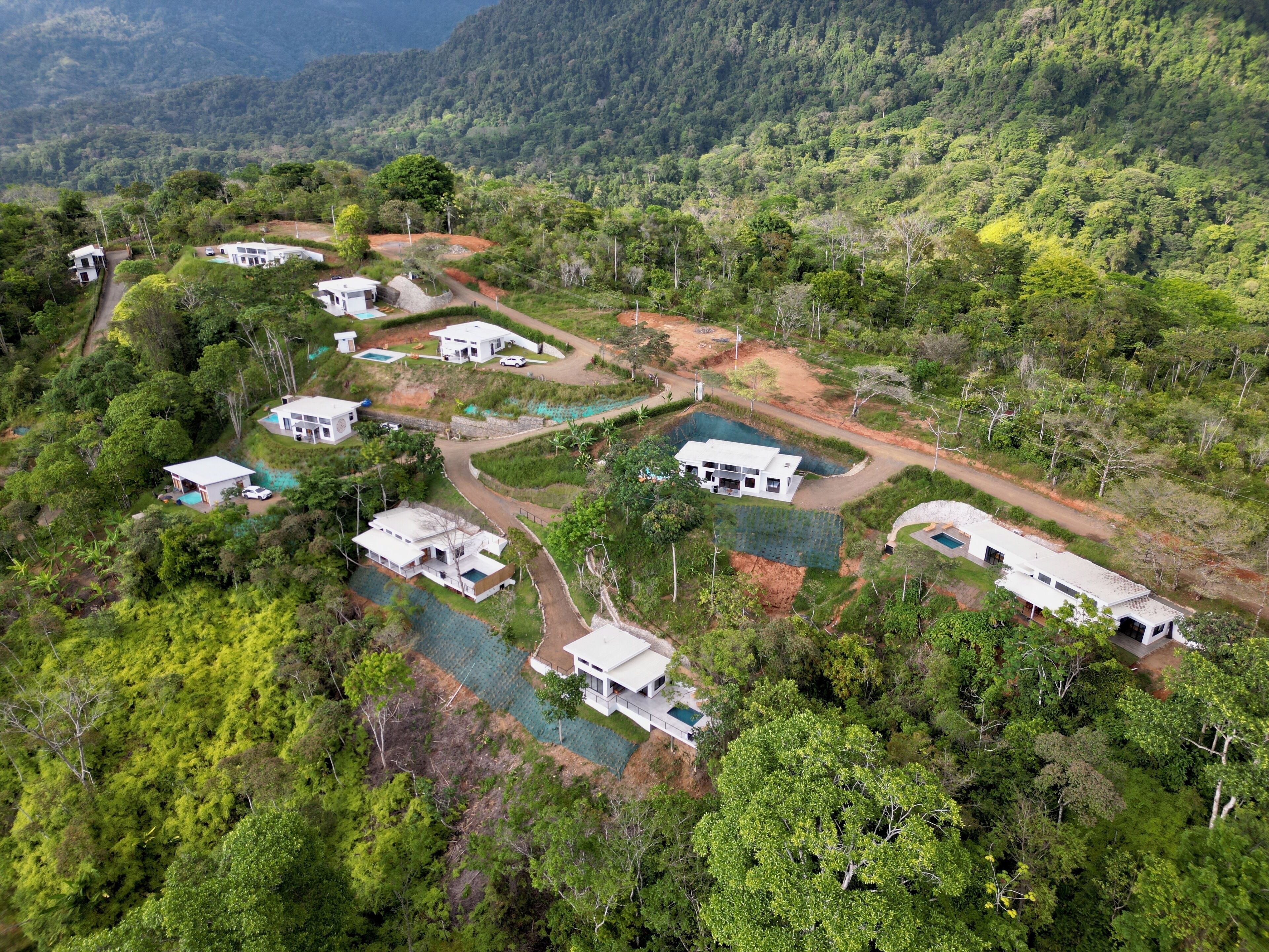 Vue aérienne d’un complexe hôtelier comprenant plusieurs bâtiments blancs, des piscines et un paysage luxuriant de forêt verdoyante.