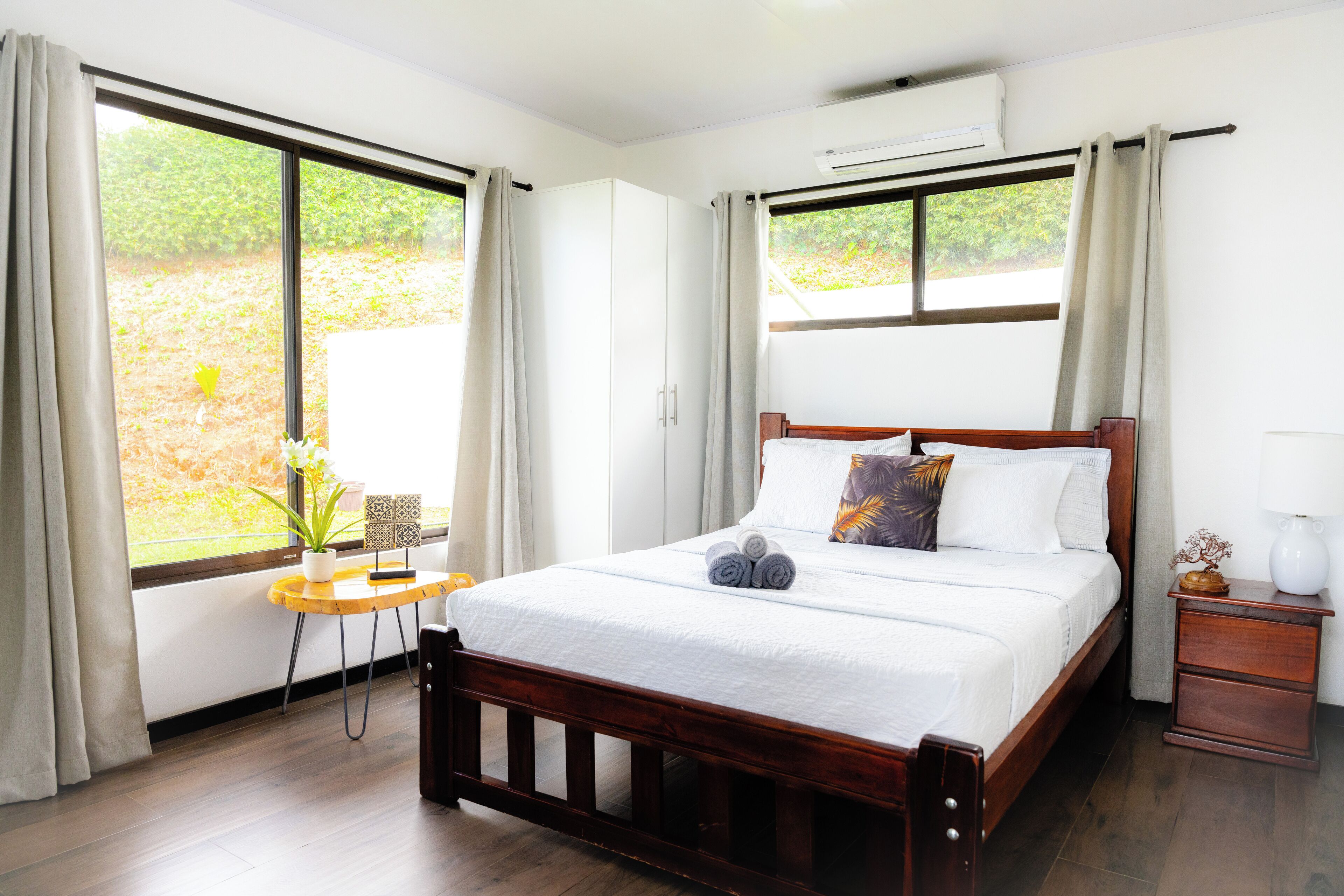 Un dormitorio con una cama de madera, una mesita con una planta y una mesilla de noche con una lámpara.