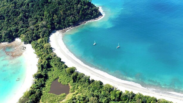 Vista aérea de una isla tropical con playa de arena blanca, aguas turquesas cristalinas y exuberante bosque verde.