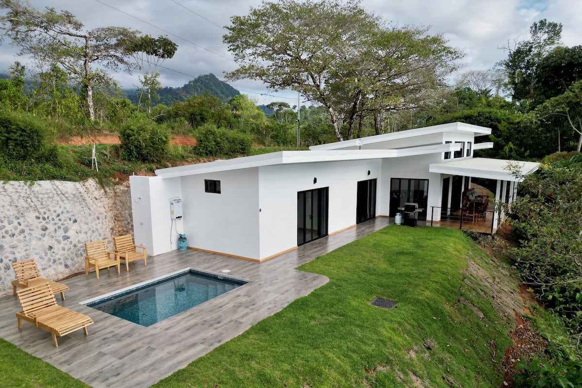 A modern house with a swimming pool, a covered patio, and a view of a mountain.