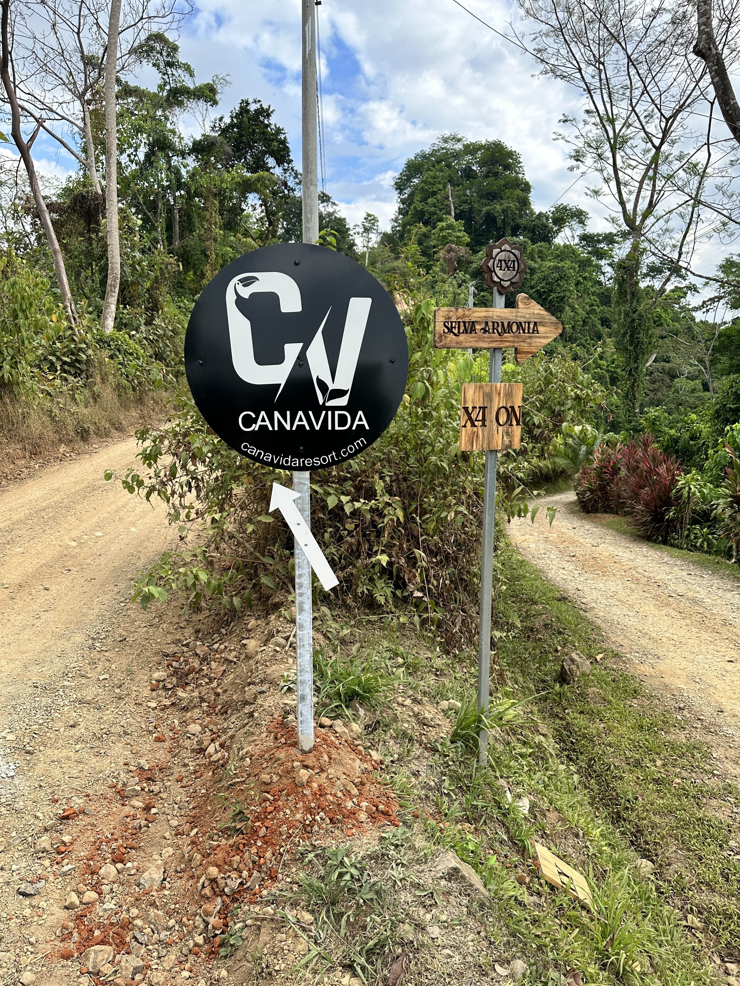 A signpost with directions to 'CANAVIDA' and 'SRIMA ARMONIA' with a dirt road in the background.