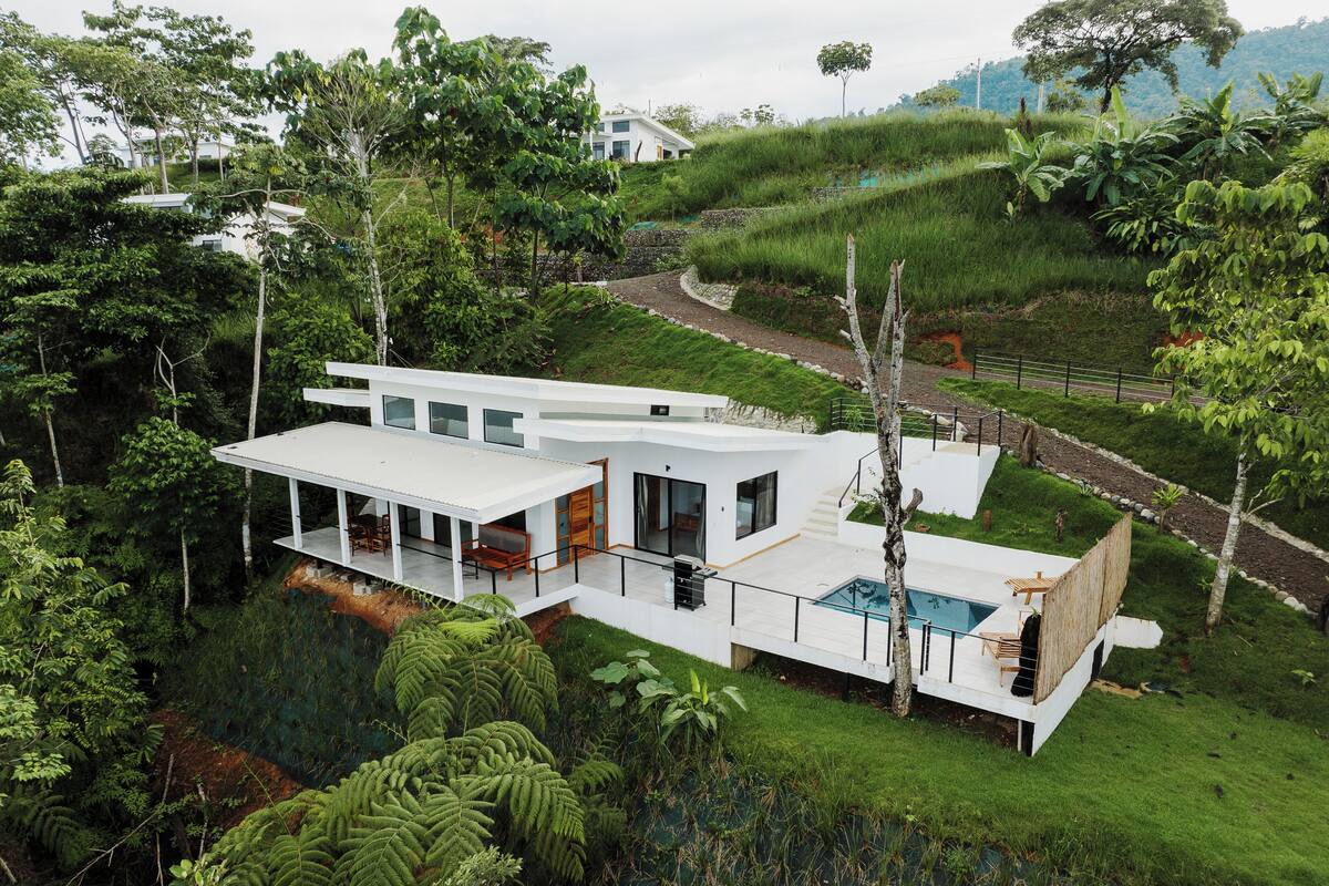 A modern house with a large deck, a swimming pool, and lush greenery surrounding it.