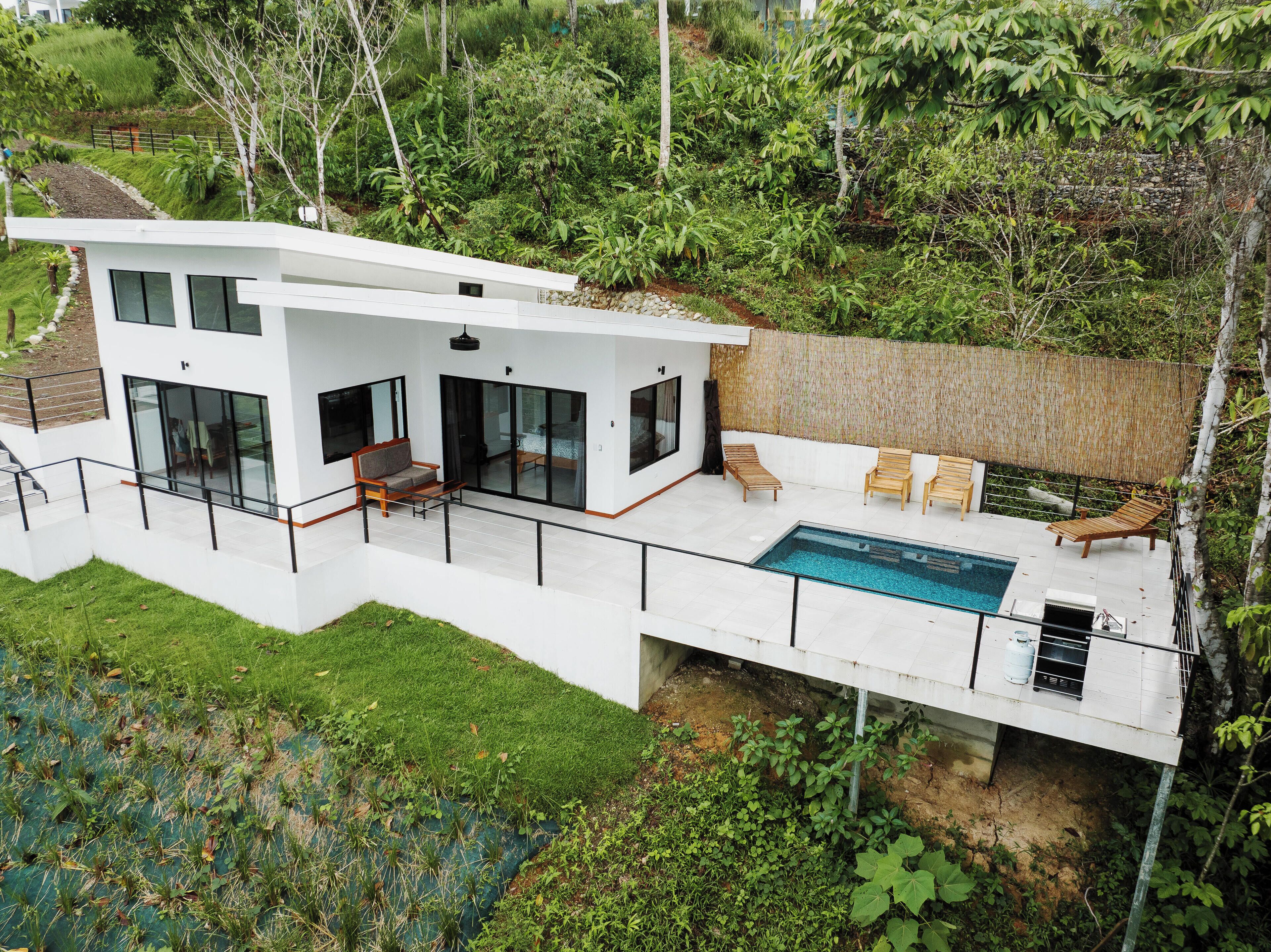 A modern house with a large balcony, a swimming pool, and lush greenery.