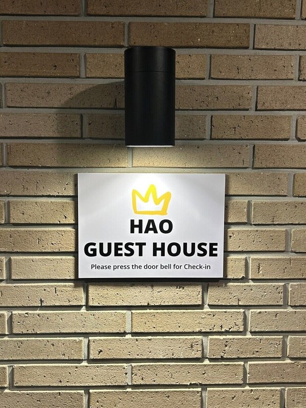 A sign for the Hao Guest House with a crown symbol and instructions to press the doorbell for check-in.