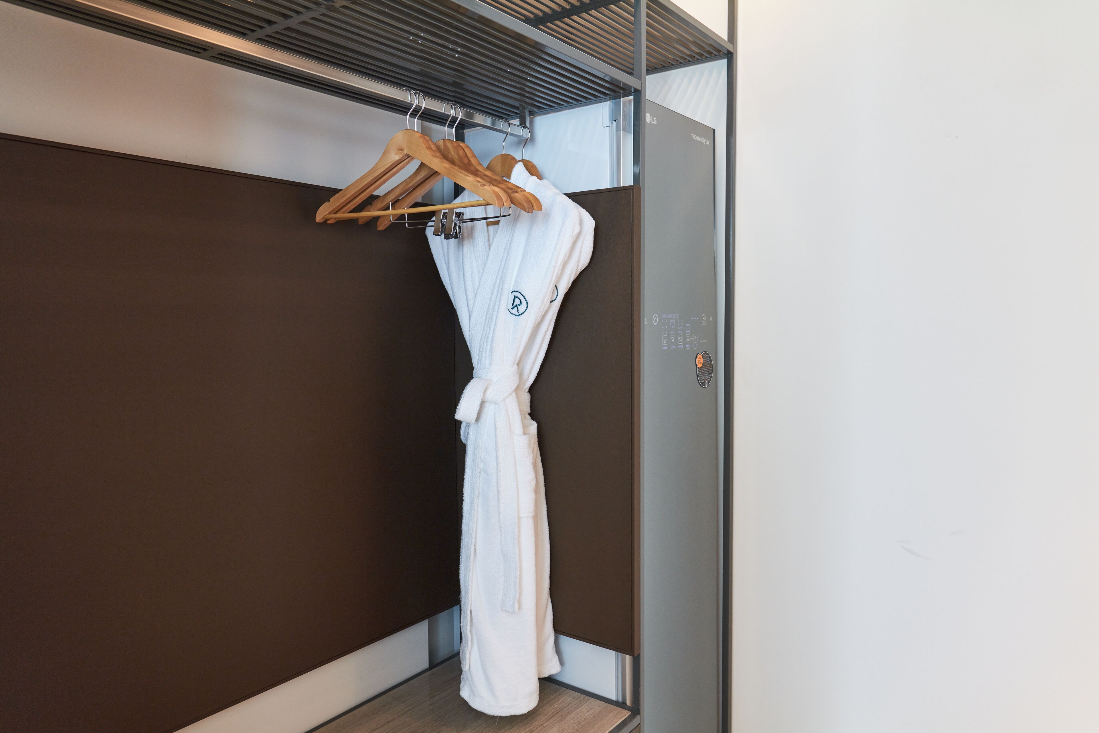Una bata blanca colgada de una percha de madera en una habitación con paredes marrones y una puerta metálica.