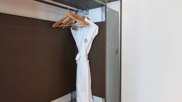 Una bata blanca colgada de una percha de madera en una habitación con paredes marrones y una puerta metálica.