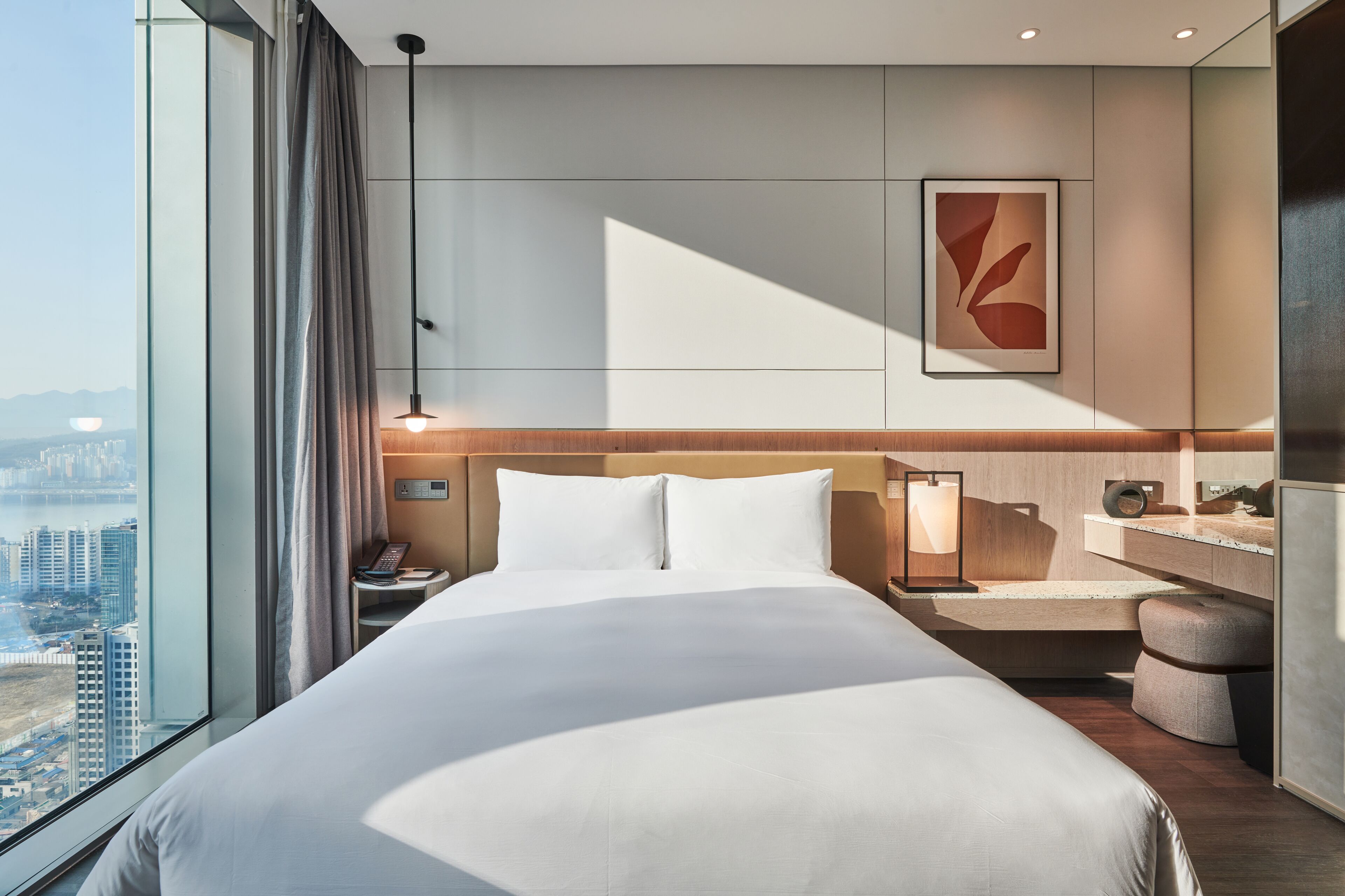 Habitación de hotel moderna con una cama grande, mesita de noche, lámpara y vistas a la ciudad.