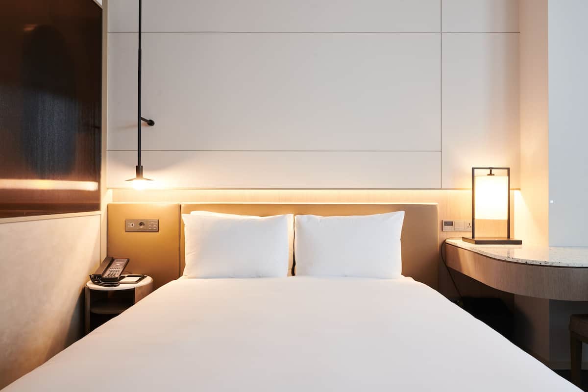 A hotel room with a bed, bedside table, lamp, and phone.