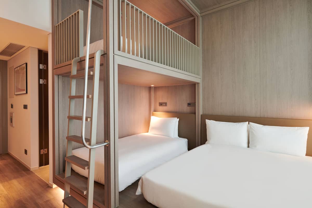 A hotel room with a bunk bed, a separate bed, and a staircase leading to a balcony.