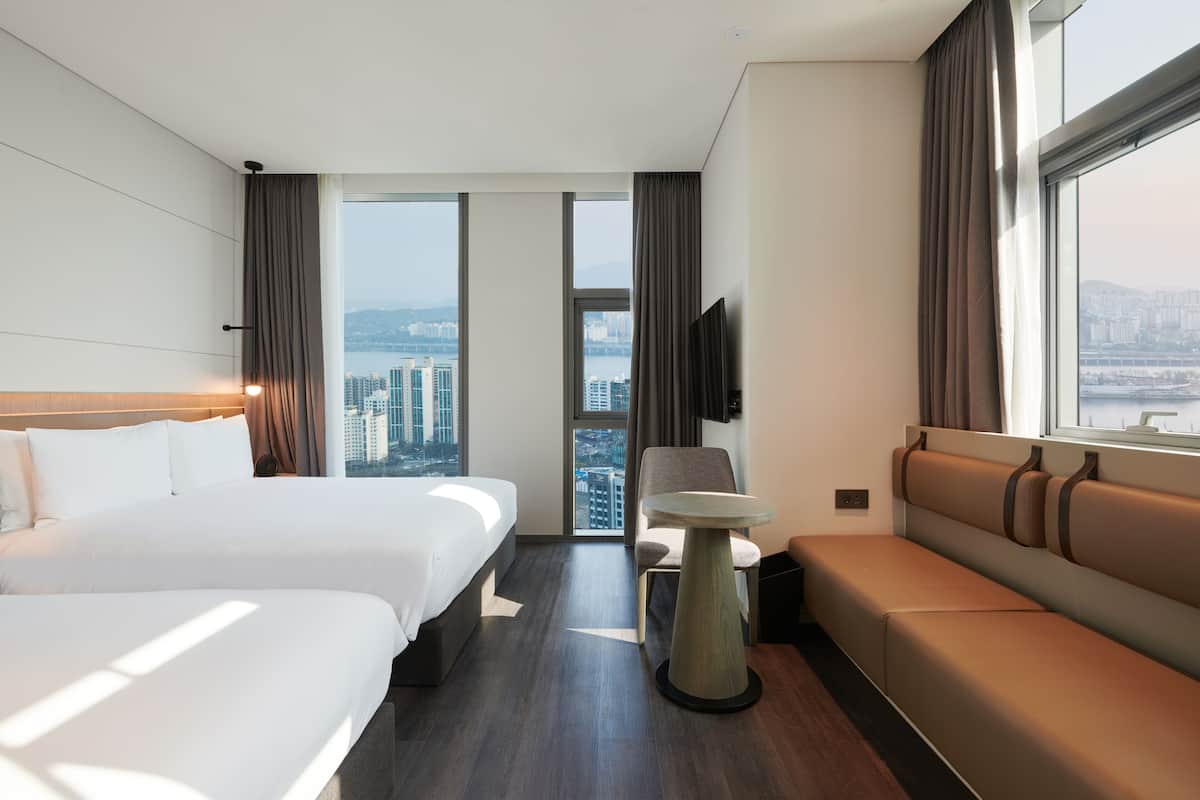 A hotel room with two beds, a sofa, a small table, and a TV.