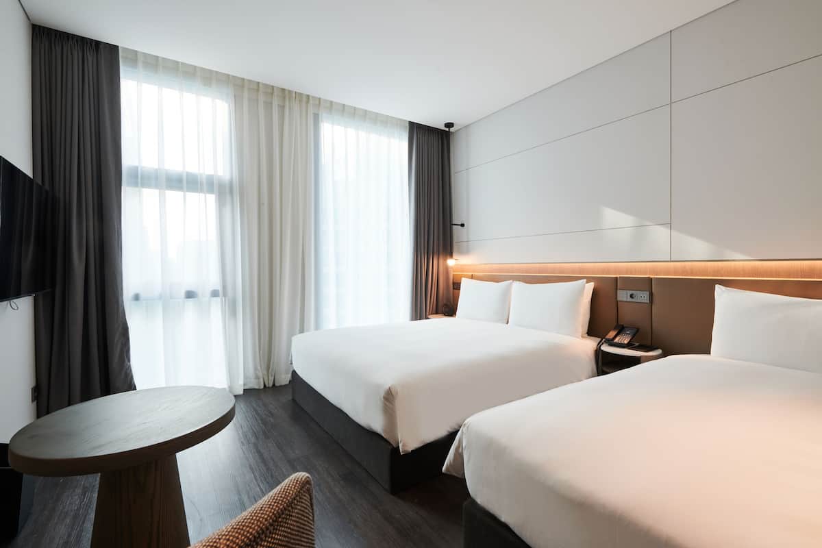 A hotel room with two beds, a small round table, a TV, and a bedside table with a phone.
