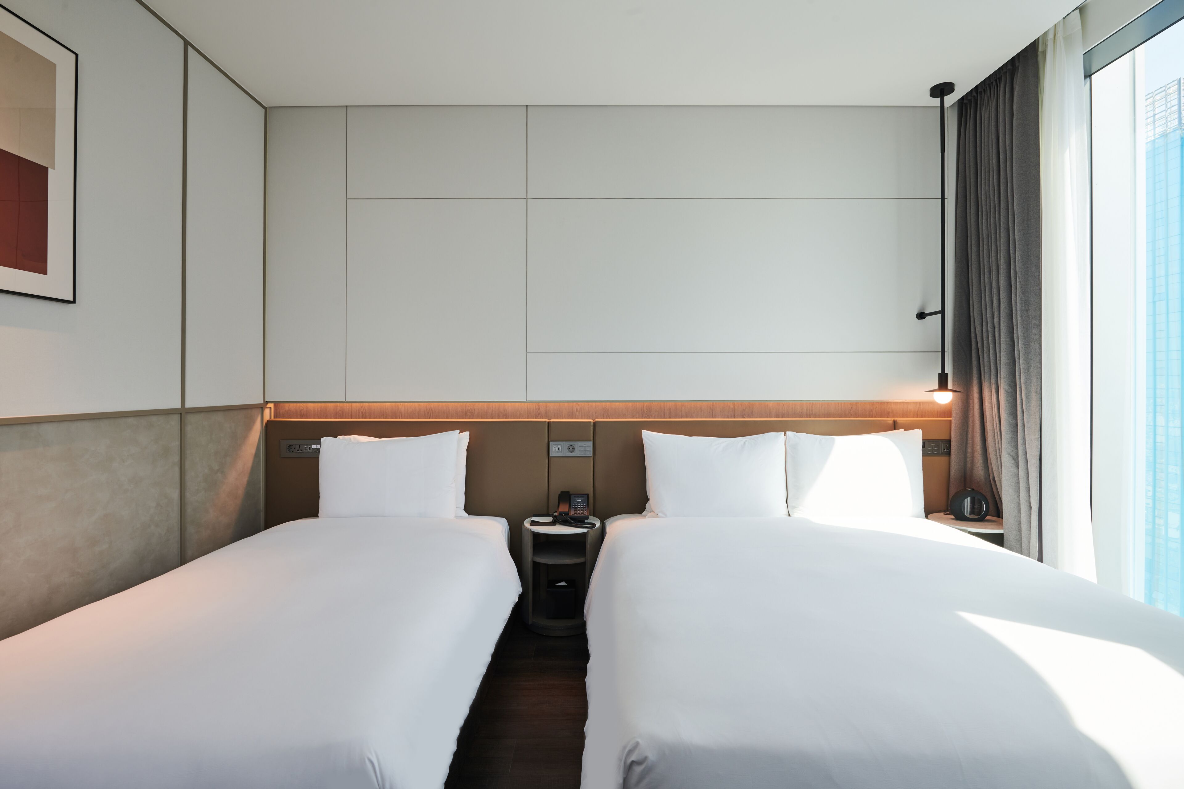 A hotel room with two beds, a nightstand with a phone, and a window with curtains.