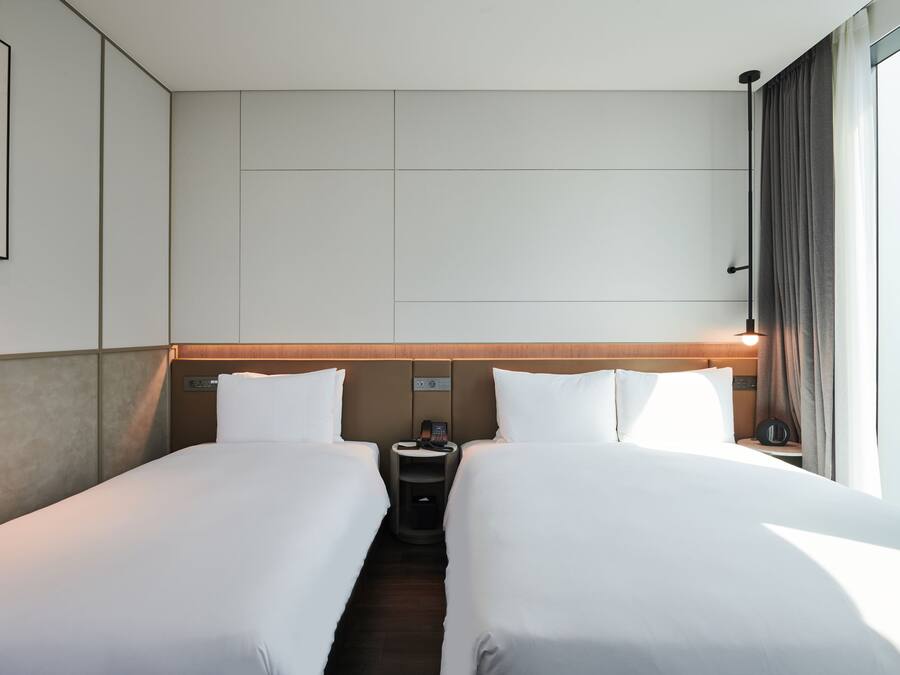 Habitación de hotel con dos camas, una mesita de noche con teléfono y una ventana con cortinas.