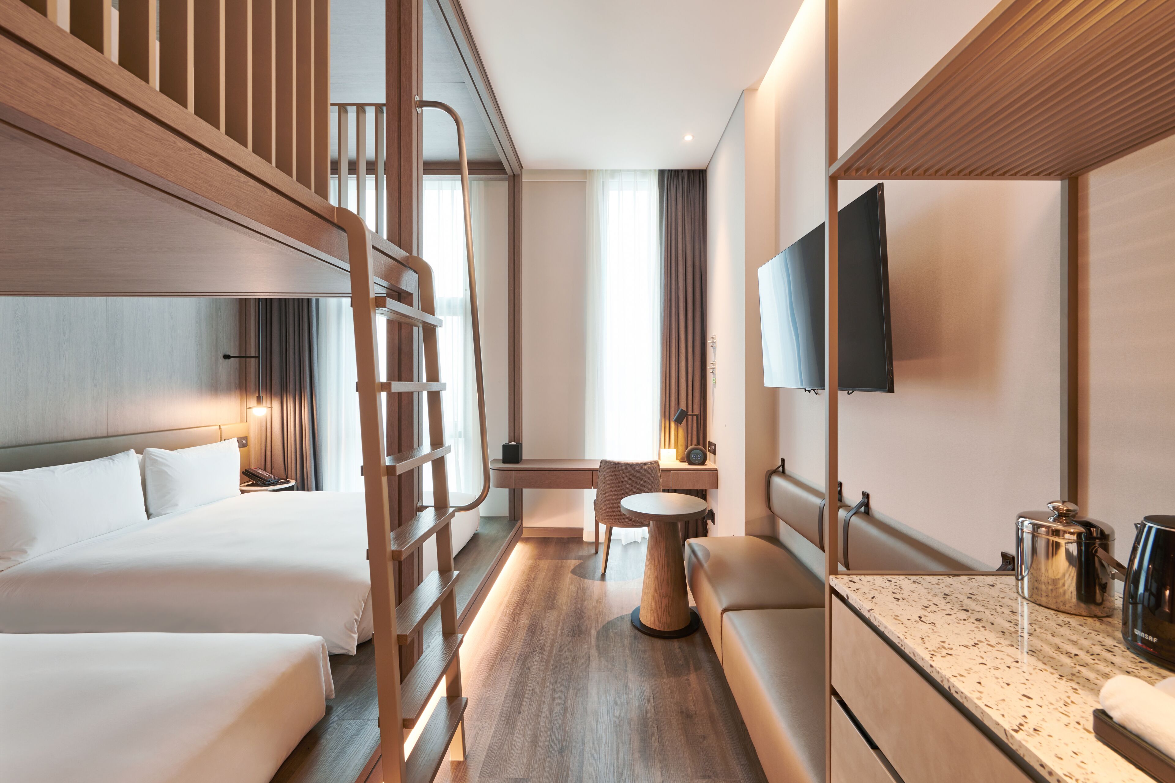 A hotel room with two beds, a desk, a chair, a TV, and a coffee maker.