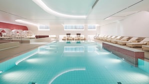 A modern indoor swimming pool with lounge chairs and a red wall.
