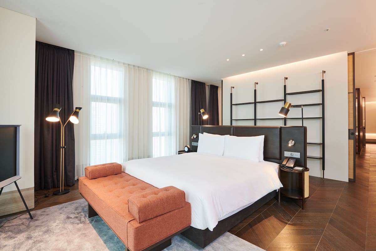 A modern hotel room with a large bed, a seating area, a desk, and a TV.