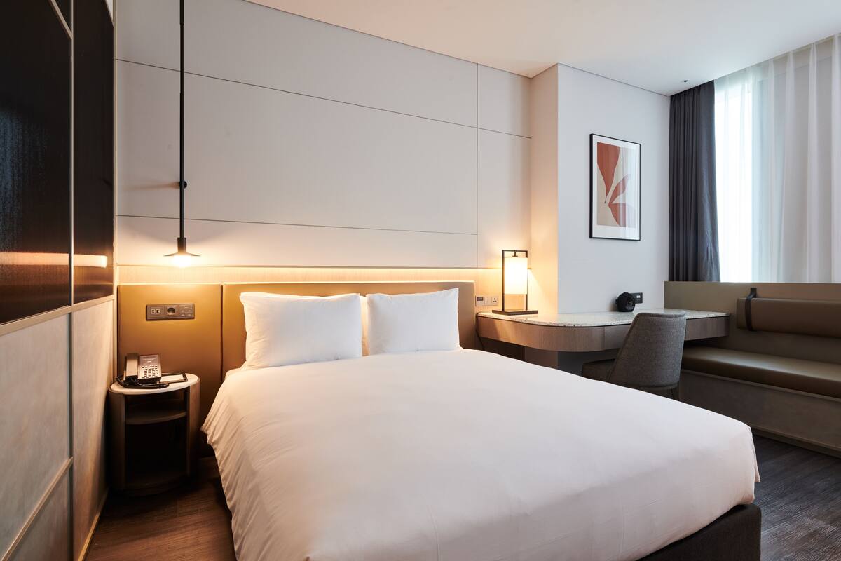 A hotel room with a large bed, bedside table, lamp, and a sofa.