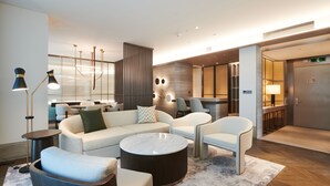 A modern hotel lobby with a sectional sofa, armchairs, a round coffee table, and a bar area.