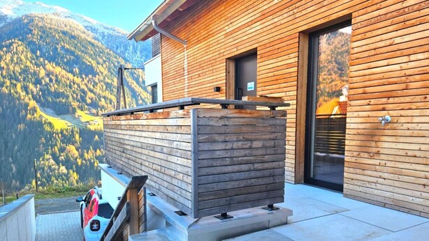 A wooden cabin with a stone staircase leading to a deck, overlooking a mountainous landscape.